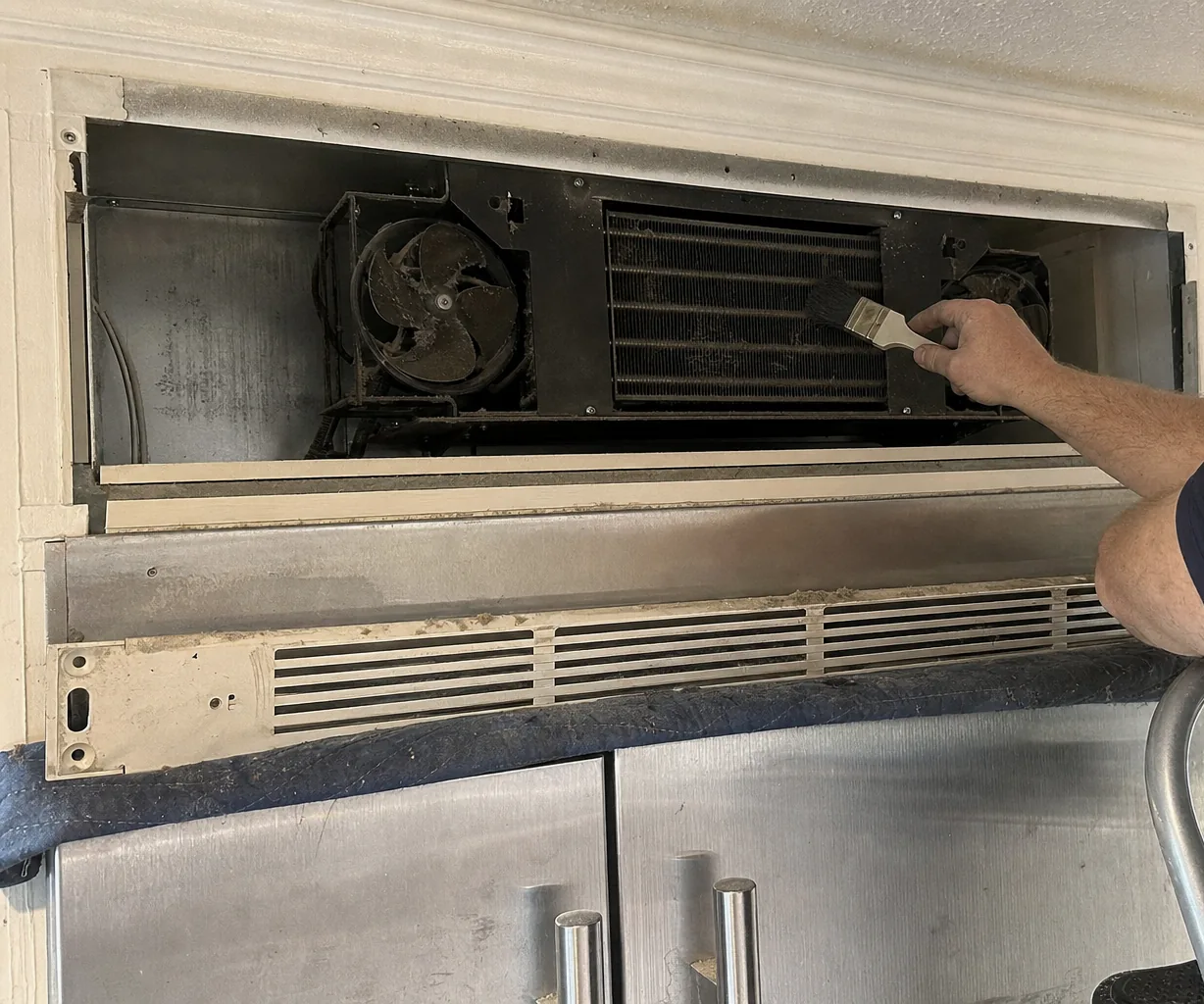 The left side of an exposed condenser deck: a dust-caked fan in its shroud and the cable run that leaves the compartment toward the cabinet wall.